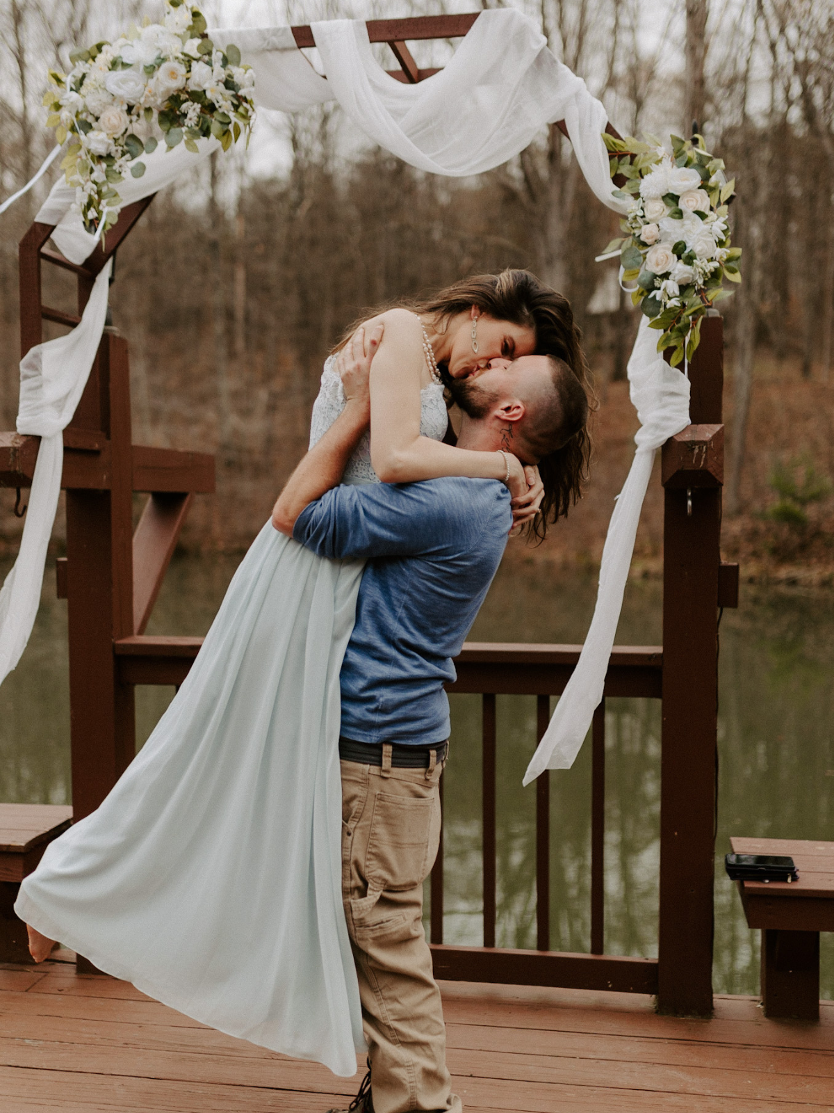 Bride bring picked up and kissed by groom, in front of a decorated archway